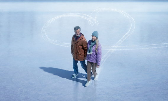Man and woman ice skating in front of a heart shape on the ice